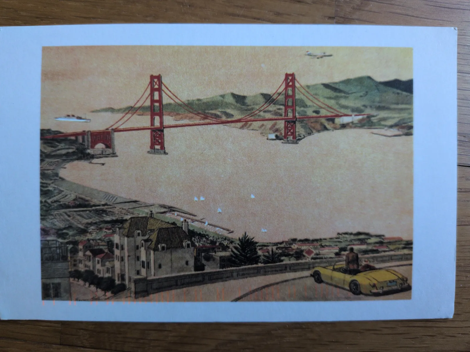 Das Bild zeigt die rote Golden Gate Bridge über einer Bucht, eine Stadt im Vordergrund und ein gelbes Cabrio auf einer kurvigen Straße.