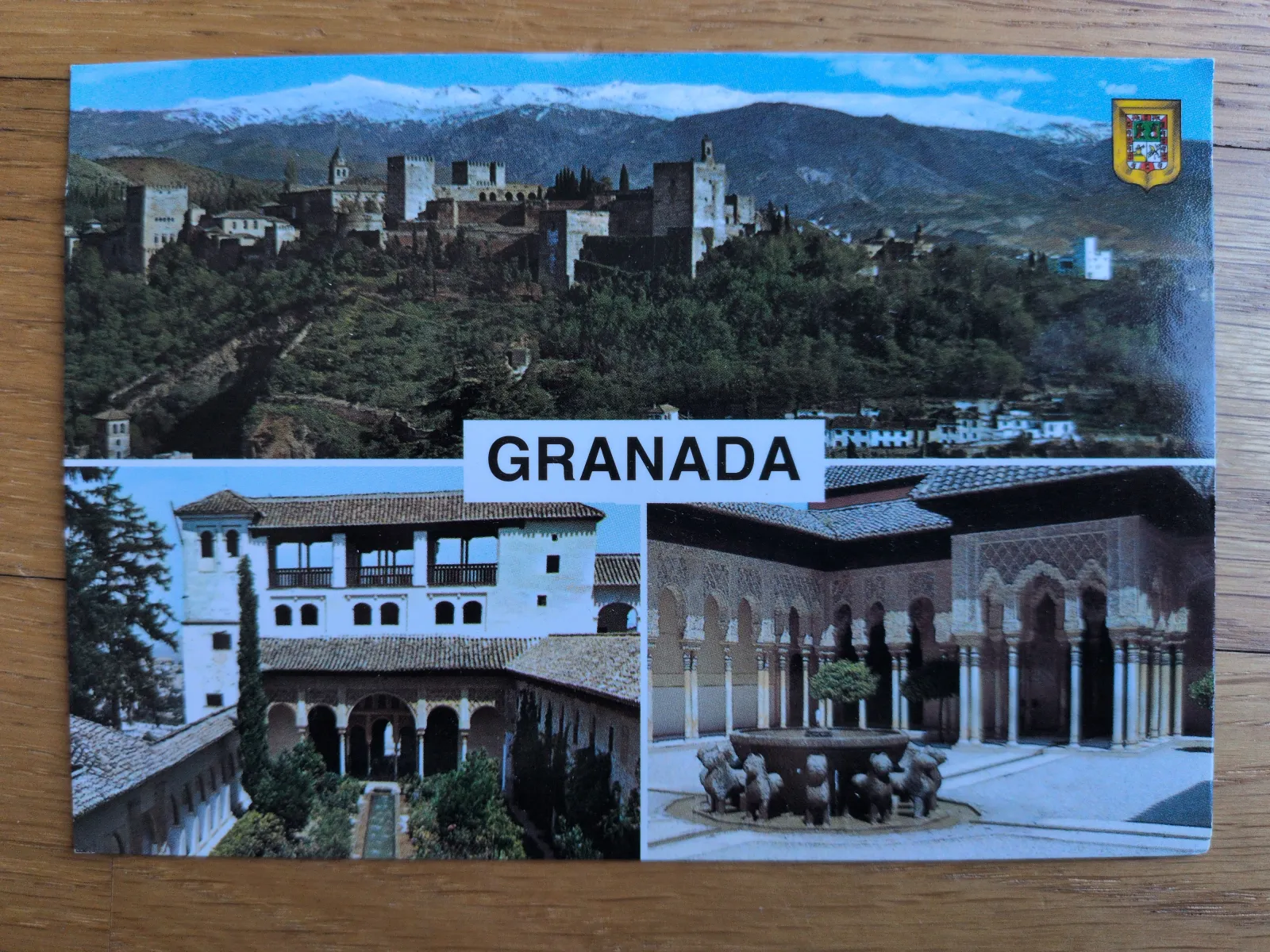 Eine Postkarte zeigt eine Collage von Granada mit der Alhambra vor schneebedeckten Bergen und dem berühmten Löwenbrunnen.