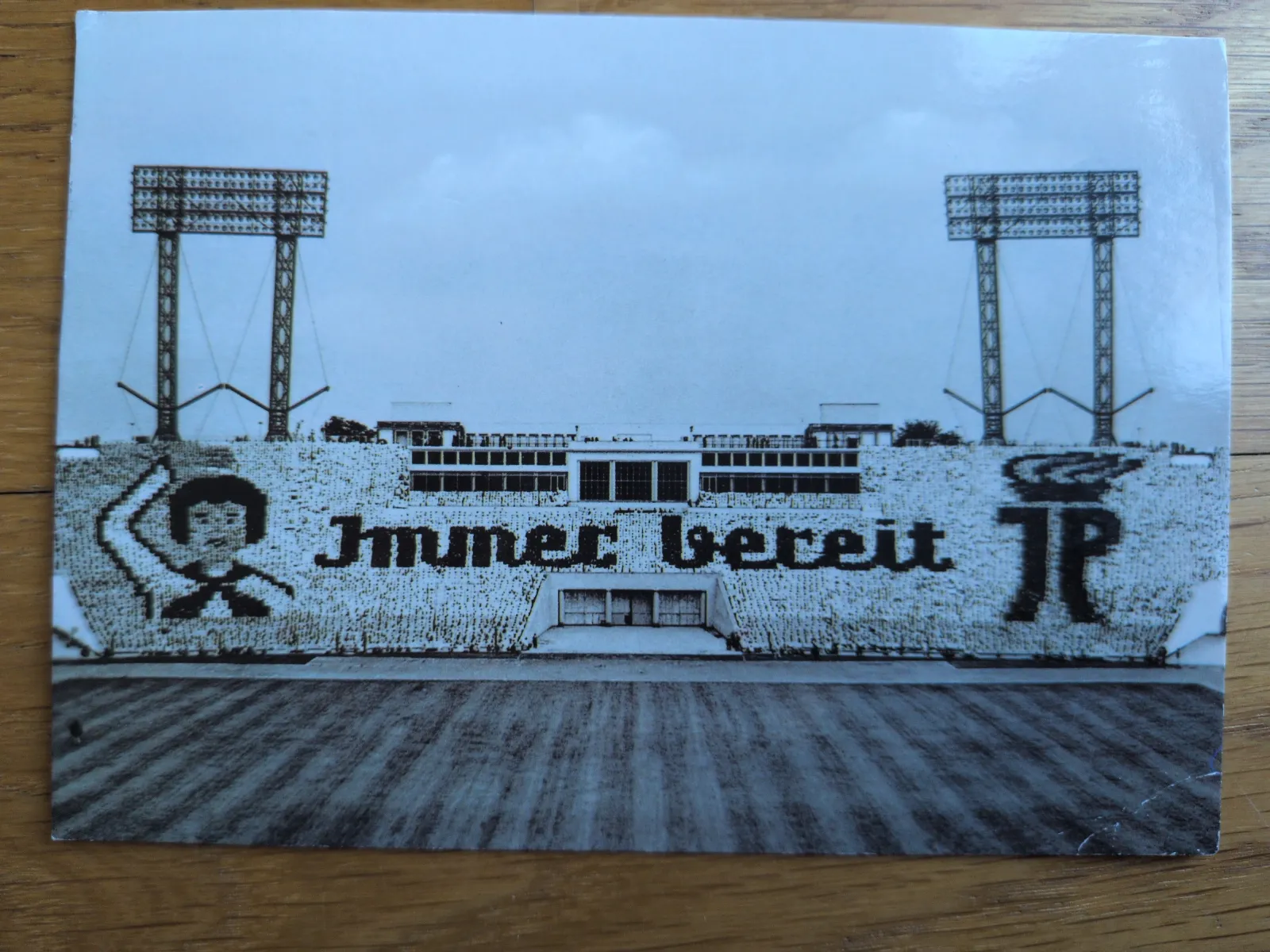 Zuschauer in einem Stadion bilden auf den Tribünen die Botschaft „Immer bereit“, die Initialen „JP“ und eine Figur eines jungen Pioniers.