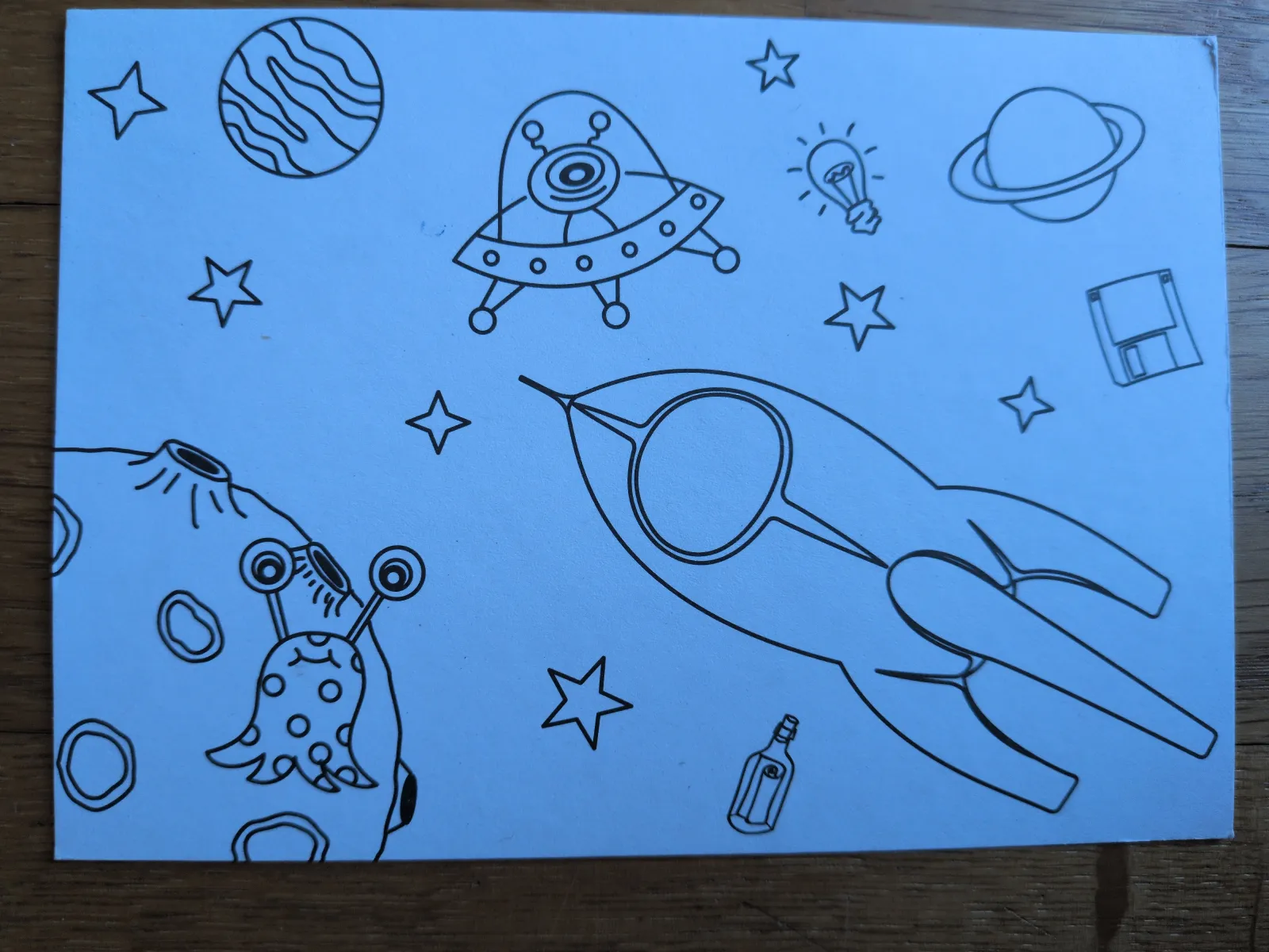 Eine blaue Zeichnung mit schwarzen Umrissen zeigt eine Rakete, Planeten, Sterne, ein UFO und ein Alien.