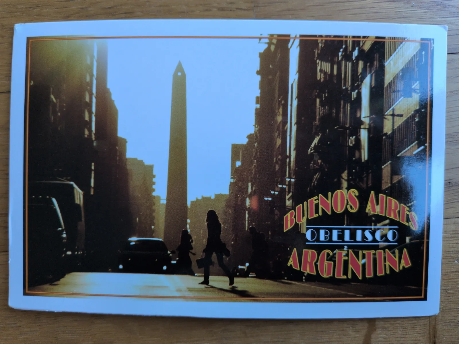 Das Bild zeigt den Obelisken von Buenos Aires in Argentinien, eingerahmt von dunklen Hochhäusern, mit schemenhaften Menschen und dem Schriftzug "BUENOS AIRES OBELISCO ARGENTINA".