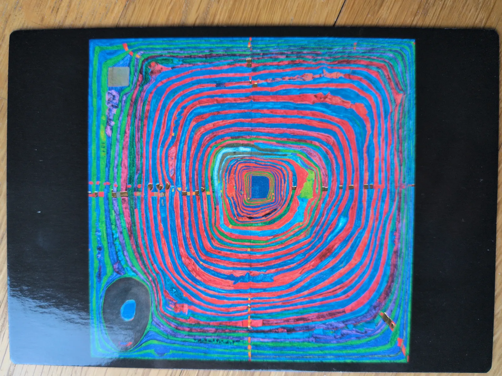Ein abstraktes, farbenfrohes Muster aus konzentrischen roten und blauen Wellenlinien, die sich zu einem Quadrat in der Mitte verengen, auf schwarzem Hintergrund.