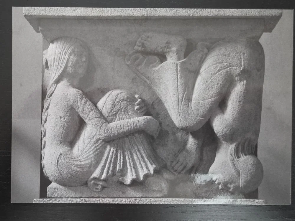 Ein steinernes Relief zeigt eine sitzende Meerjungfrau mit langem Zopf und ein geflügeltes Wesen.