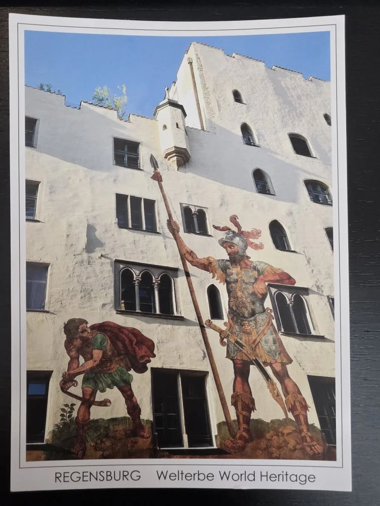 Ein großes Wandgemälde auf der weißen Fassade des Regensburger Goliathhauses zeigt den biblischen Kampf zwischen dem riesigen, gerüsteten Goliath mit einer Lanze und dem kleineren David.