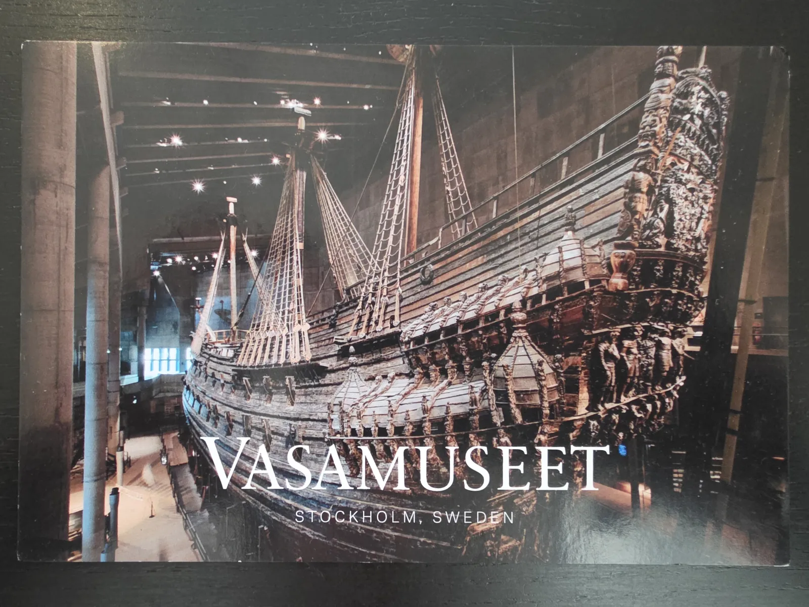 Eine Aufnahme des monumentalen, historischen Holzschiffs Vasa im Vasamuseet in Stockholm, überlagert mit dem weißen Schriftzug „VASAMUSEET STOCKHOLM, SWEDEN“.