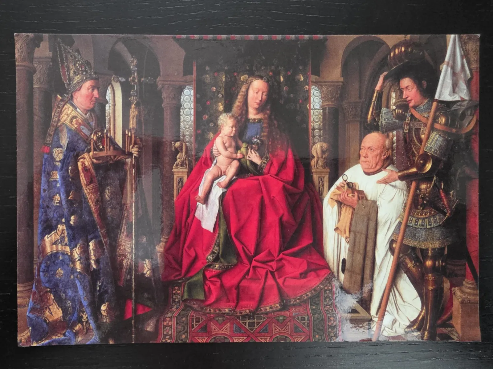 Ein klassisches Renaissance-Gemälde zeigt die thronende Jungfrau Maria im roten Gewand mit dem Jesuskind, flankiert von Heiligen und einem knienden Stifter in einer prachtvollen Kirche.