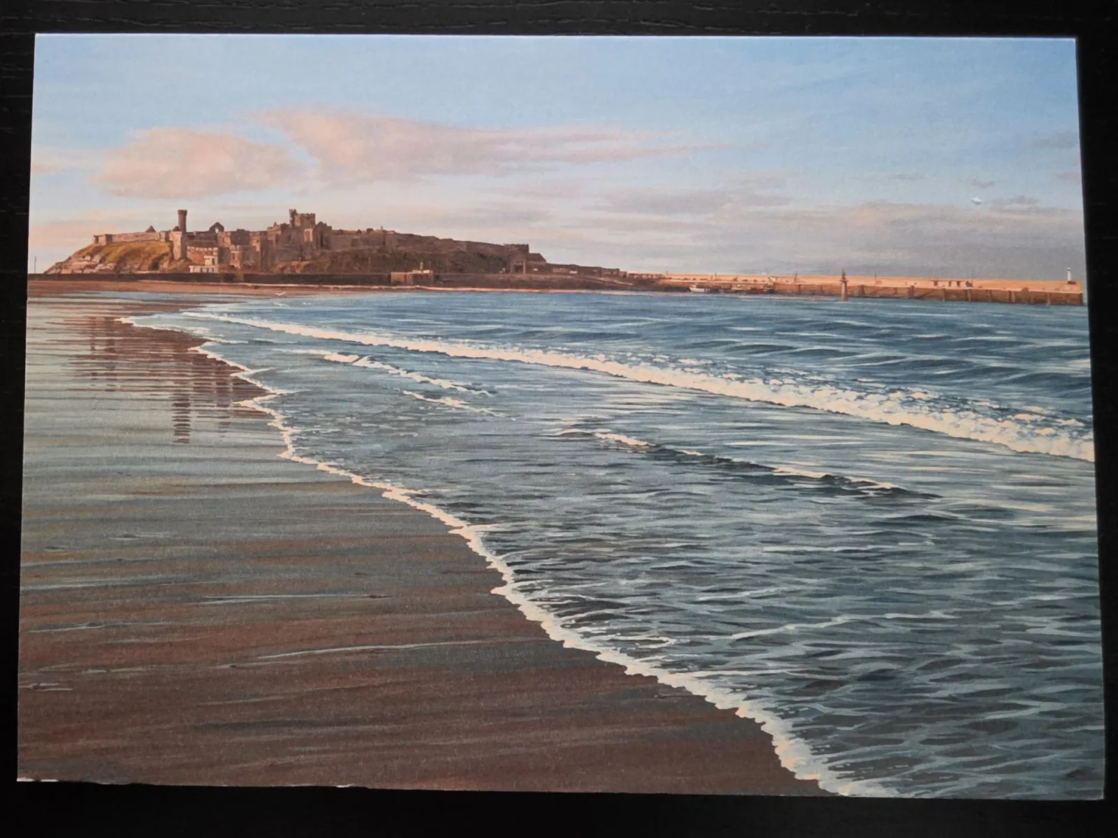Ein Gemälde zeigt sanfte Meereswellen, die an einen nassen Sandstrand spülen, während im Hintergrund eine historische Burgruine auf einer Landzunge im warmen Abendlicht thront.