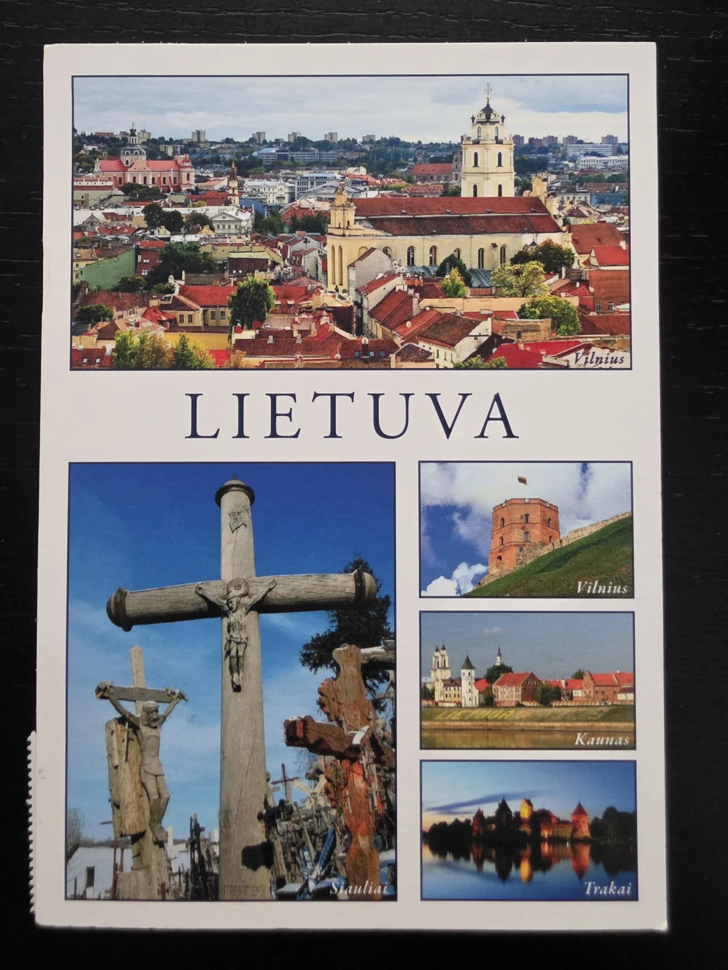 Eine Postkarte mit dem Schriftzug „LIETUVA“ zeigt eine Collage aus fünf Bildern bekannter litauischer Sehenswürdigkeiten, darunter die Altstadt von Vilnius, der Berg der Kreuze in Šiauliai und die Burg Trakai.