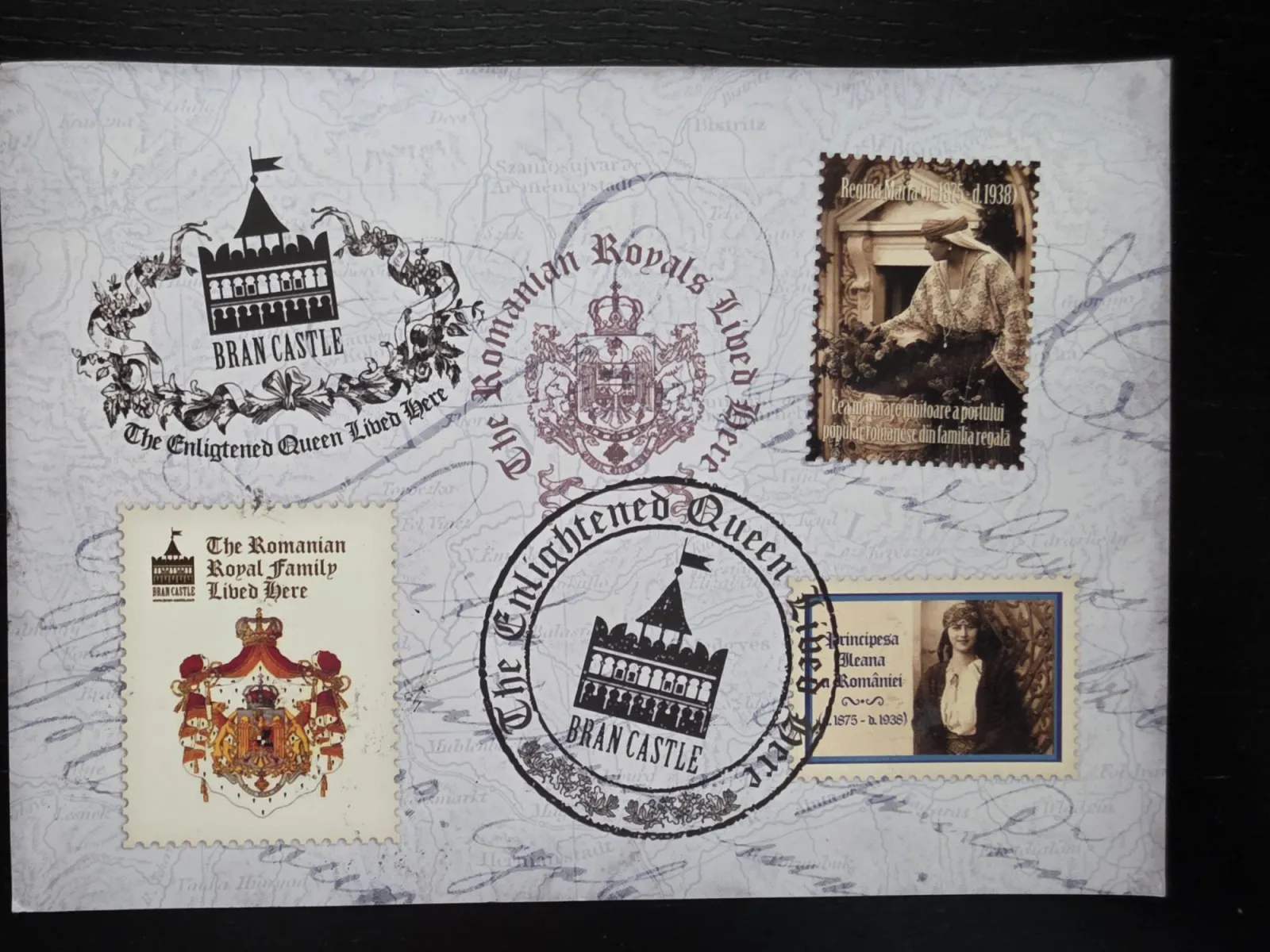 Eine collageartige Postkarte mit dem Hintergrund einer historischen Landkarte zeigt verschiedene Briefmarken und Stempel, die Schloss Bran und der rumänischen Königsfamilie gewidmet sind.