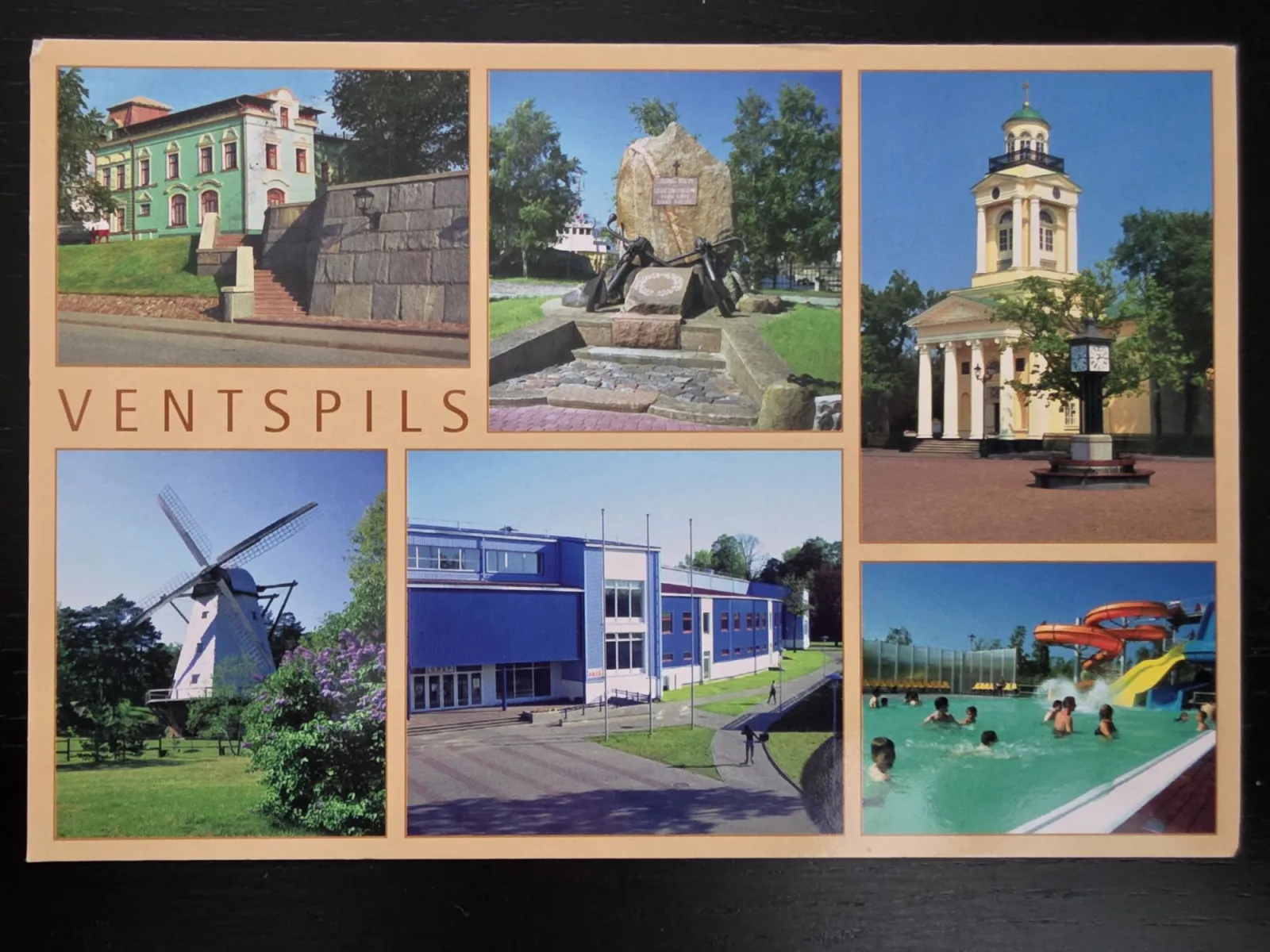 Eine Postkarte der Stadt Ventspils zeigt eine Collage aus sechs Bildern mit lokalen Sehenswürdigkeiten wie einer Windmühle, einer Kirche, einem Denkmal und einem Freibad.