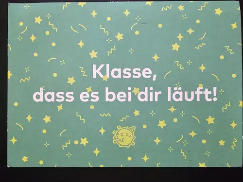 Eine grüne Karte mit gelben Konfetti-Motiven zeigt den weißen Text "Klasse, dass es bei dir läuft!" und ein lachendes Party-Sonne-Symbol.