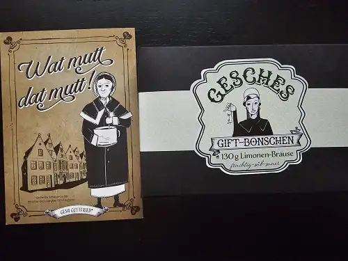 Eine braune Karte mit einer altmodisch gekleideten Frau und dem Namen "Gesa Gottfried" liegt neben einer schwarzen Geschenkbox mit einem Etikett für "Gesches Gift-Bonschen".