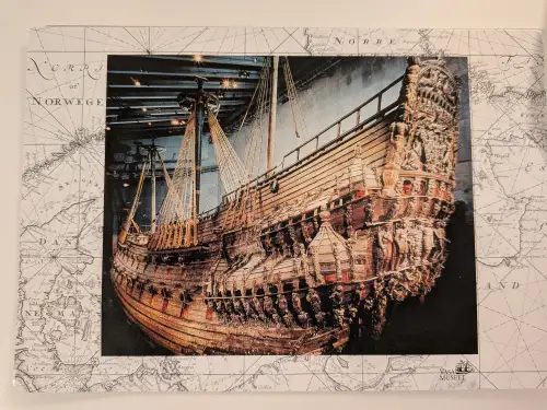 Ein großes, reich geschnitztes Holzschiff, die Vasa, ist in einem Museum ausgestellt und von einer historischen Seekarte umgeben.