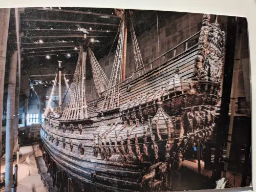 Ein riesiges, reich verziertes Holzschiff mit hohen Masten steht in einem dunklen Museumssaal.