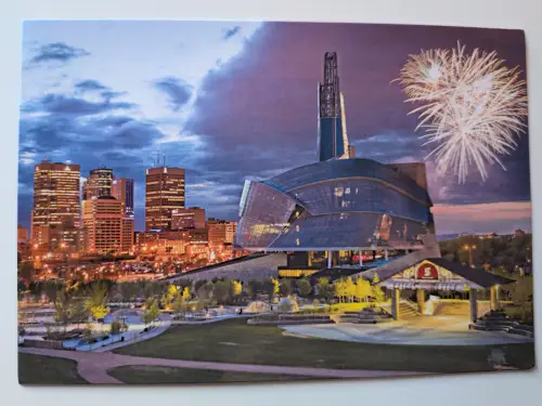 Ein markantes, geschwungenes Gebäude mit hohem Turm dominiert eine nächtliche Stadtlandschaft mit beleuchteter Skyline und Feuerwerk am Nachthimmel.