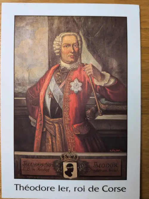 Ein historisches Porträtgemälde zeigt Théodore I., König von Korsika, in rotem Ornat, weißer Perücke und mit Zepter.