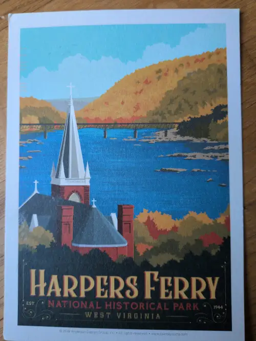 Ein Vintage-Poster zeigt eine Kirche mit spitzem Turm im Vordergrund, dahinter einen Fluss mit Brücke und herbstlich gefärbten Bäumen, sowie den Schriftzug "Harpers Ferry National Historical Park".