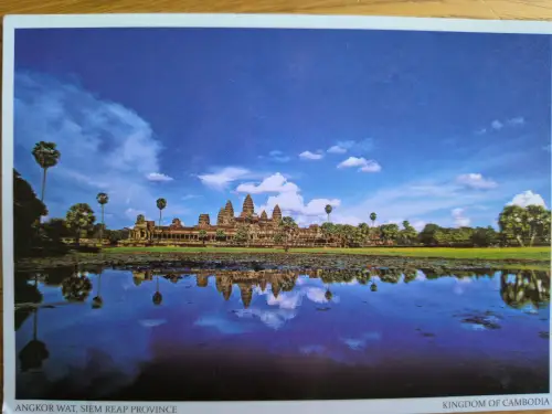 Angkor Wat mit seinen Türmen und Palmen spiegelt sich unter blauem Himmel in einem See.
