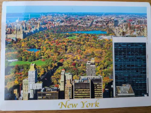 Das Bild ist eine Luftaufnahme von New York City mit dem herbstlich bunten Central Park, umgeben von Wolkenkratzern.