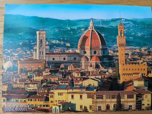 Ein Panorama von Florenz, dominiert vom roten Dom und seinen Türmen, umgeben von der Altstadt mit Terrakottadächern und grünen Hügeln im Hintergrund.