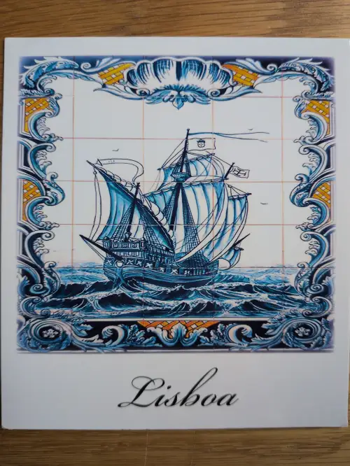 Ein blau-weißes Azulejo-Bild zeigt ein Segelschiff auf hohen Wellen, umrahmt von Ornamenten, mit dem Schriftzug "Lisboa" am unteren Rand.