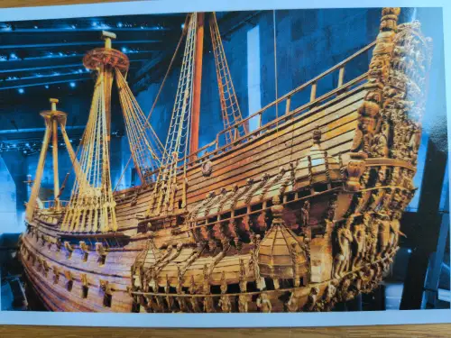 Ein prunkvolles, altes Holzschiff mit hohen Masten und reichen Schnitzereien am Heck ist in einem bläulich beleuchteten Museum ausgestellt. Das Bild zeigt die Vasa.