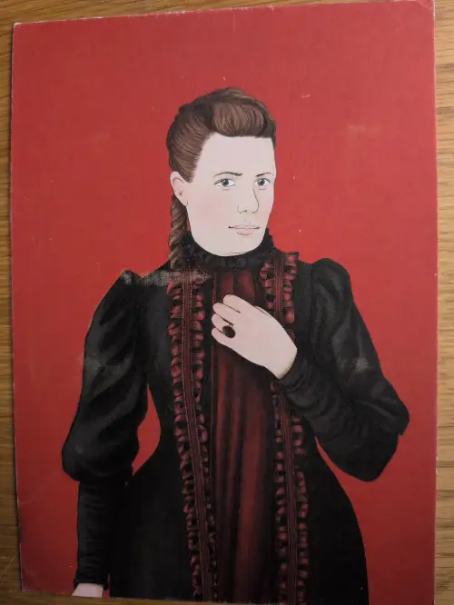 Porträt einer Frau mit braunem Haar in schwarzem Kleid mit roten Akzenten, die eine Hand mit Ring auf die Brust legt, vor rotem Grund.