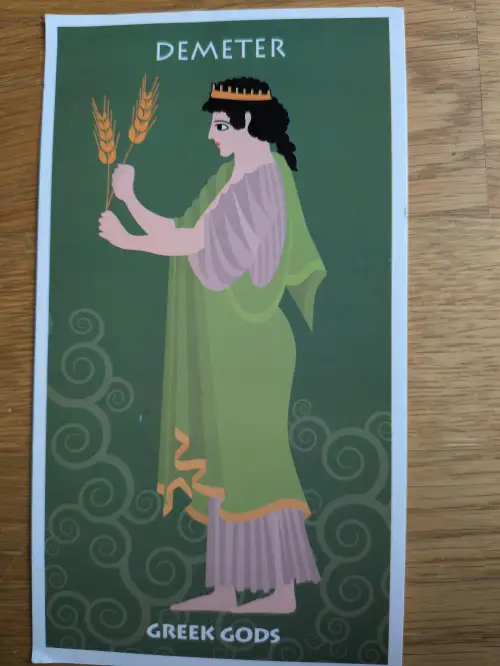 Eine stilisierte Illustration der Göttin Demeter mit goldener Krone, grünem Gewand und zwei Weizenähren in den Händen.