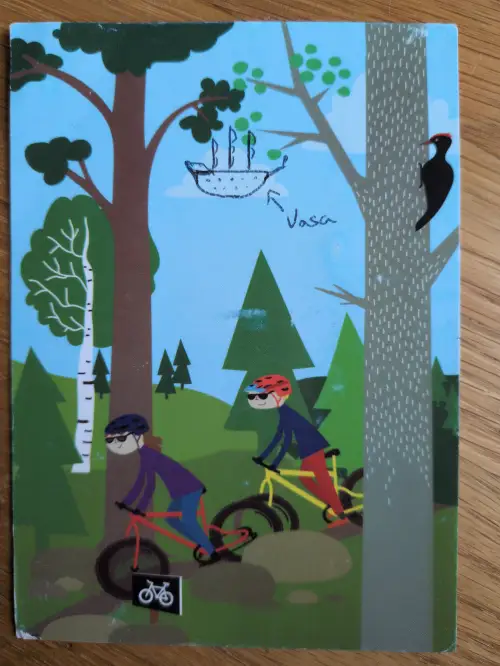 Eine bunte Cartoon-Illustration zeigt zwei Mountainbiker in einem Wald mit Bäumen und einem Specht, darüber ein gezeichnetes Schiff mit dem Schriftzug 'Vasa'.