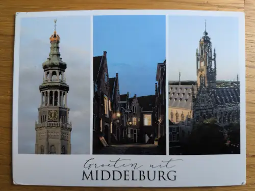 Eine Postkarte zeigt drei Stadtansichten von Middelburg: links einen hohen Kirchturm, in der Mitte eine abendliche Gasse mit beleuchteten Häusern und rechts ein historisches Gebäude mit spitzem Turm.