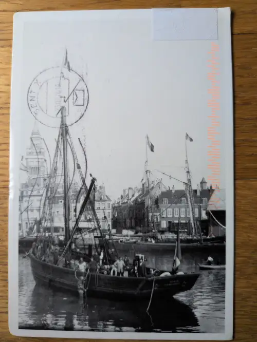 Schwarz-Weiß-Foto einer Hafenszene mit Segelschiffen und Stadtkulisse, versehen mit einem Poststempel oben links und orangefarbenem Text rechts.
