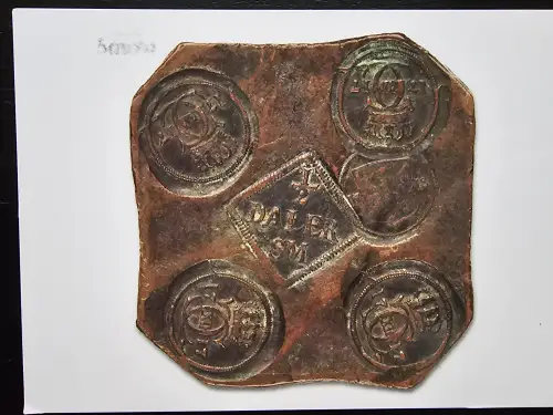 Schwedisches Kupferplatten-Geld (Plåtmynt) von 1717: Eine rechteckige Kupferplatte mit abgeschnittenen Ecken, in jeder Ecke ein geprägter Rundstempel mit dem schwedischen Reichswappen (drei Kronen), in der Mitte ein rautenförmiger Wertstempel mit '1/2 DALER S.M.' (Silvermynt). Die Patina zeigt kupfergrüne und braune Oxidation.