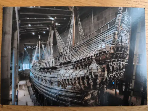 Ein riesiges, reich verziertes Holzschiff mit hohen Masten und Takelage ist in einem dunklen Museum ausgestellt.