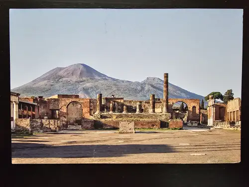 Antike Ruinen mit Säulen und dem Vesuv im Hintergrund unter klarem Himmel.