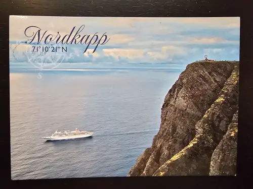 Ein Kreuzfahrtschiff fährt auf dem Meer unterhalb der imposanten Felsklippe des Nordkapps, auf der das Globus-Denkmal thront.