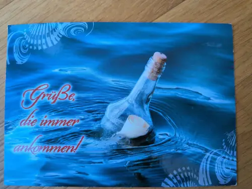 Das Bild zeigt eine Flaschenpost in dunklem, welligem Blauwasser mit dem roten Schriftzug "Grüße, die immer ankommen!".