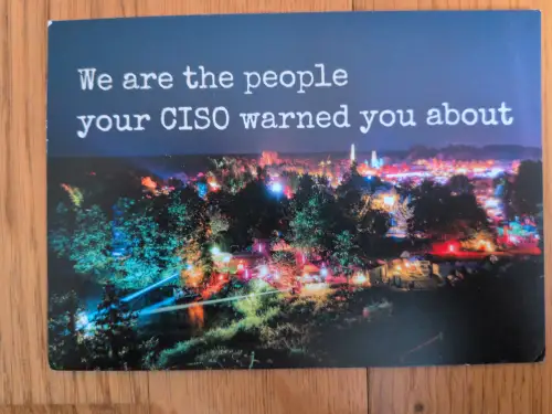 Ein Nachtbild mit leuchtenden Bäumen und bunten Lichtern einer Veranstaltung, darüber der Text: "We are the people your CISO warned you about".