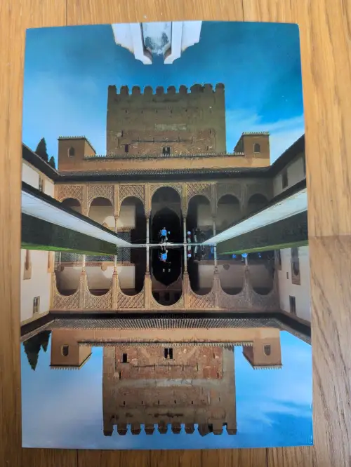 Ein maurischer Palasthof mit einem langen Wasserbecken, das die Architektur und einen Turm perfekt spiegelt.