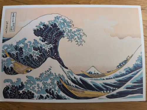 Ein japanischer Holzschnitt zeigt eine riesige, schäumende Welle, die sich über drei Fischerboote erhebt, mit dem Berg Fuji im Hintergrund.