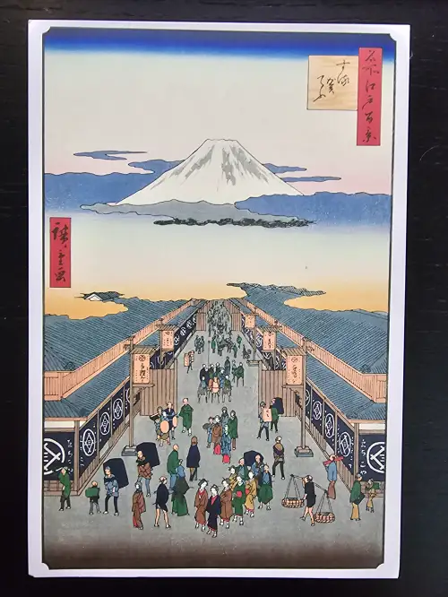 Ein japanischer Holzschnitt zeigt eine belebte Straße mit traditionellen Gebäuden und vielen Menschen, überragt vom schneebedeckten Berg Fuji.