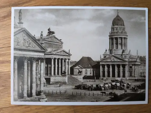 Ein historisches Schwarz-Weiß-Foto zeigt einen großen Platz mit imposanten klassizistischen Gebäuden, darunter eines mit einer Kuppel, sowie Pferdewagen und Menschen.