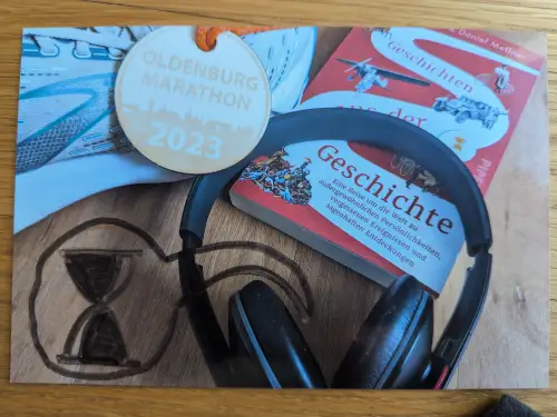 Auf einem Holzhintergrund liegen ein Laufschuh, eine Oldenburg Marathon 2023 Medaille, ein Buch mit dem Titel "Geschichte", schwarze Kopfhörer und ein gezeichnetes Sanduhr-Symbol.