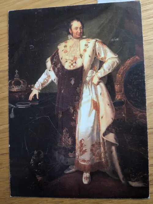 Ein Gemälde zeigt einen stehenden Mann in königlicher Robe mit Pelz und Schmuck, der eine Hand auf einen Tisch mit einer Krone legt.