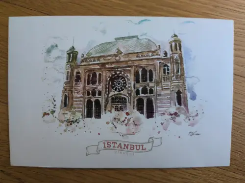 Ein Aquarellbild zeigt den historischen Bahnhof Sirkeci in Istanbul mit einer Kuppel, zwei Türmen und einem großen Rosettenfenster, darunter der Schriftzug „ISTANBUL SIRKECI“.