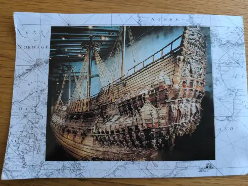 Ein historisches, reich verziertes Holzschiff, die Vasa, ist auf einer Postkarte mit Seekartenhintergrund abgebildet.