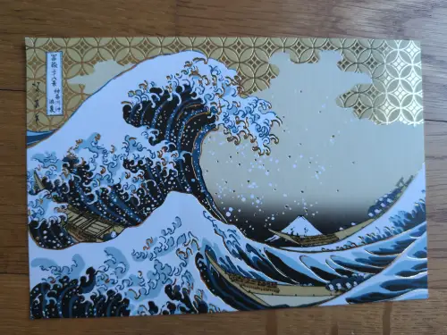 Das Bild zeigt eine stilisierte, farbige Darstellung von Hokusais „Die Große Welle vor Kanagawa“ mit großen blauen Wellen, Booten, dem Berg Fuji und goldenen Akzenten.