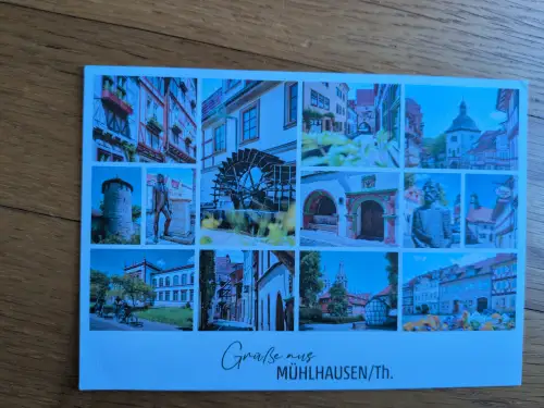 Eine Postkarte zeigt eine Collage aus zwölf Bildern mit historischen Ansichten der Stadt Mühlhausen/Th., darunter Fachwerkhäuser, ein Wasserrad und Statuen.