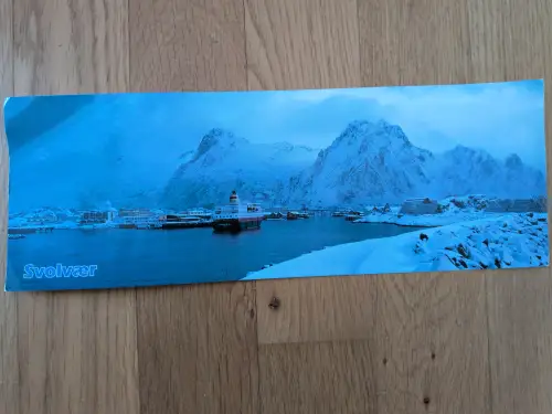 Ein winterliches Panorama der Stadt Svolvær mit schneebedeckten Bergen, einem Fjord und einem im Hafen liegenden Hurtigruten-Schiff.