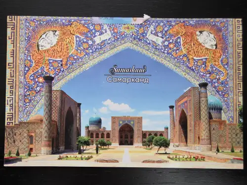 Eine Postkarte zeigt den historischen Registan-Platz in Samarkand, eingerahmt von einem kunstvollen, blauen Mosaikbogen mit Tigern und Sonnenmotiven.